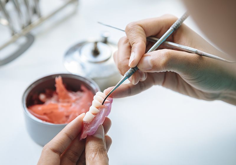 Un primer plano de manos trabajando en una dentadura postiza.